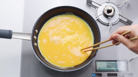 Mixing Japanese omelette egg mixture in a frying pan.