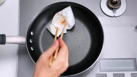 Wiping out oil and debris from frying pan with paper towels.