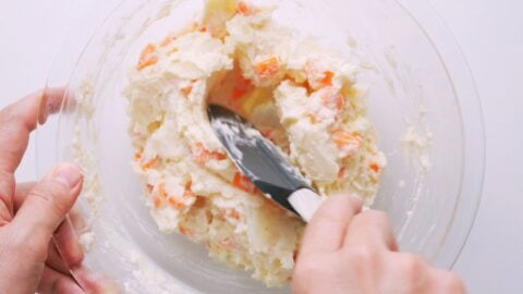 Mixing potatoes and carrots with potato salad dressing.