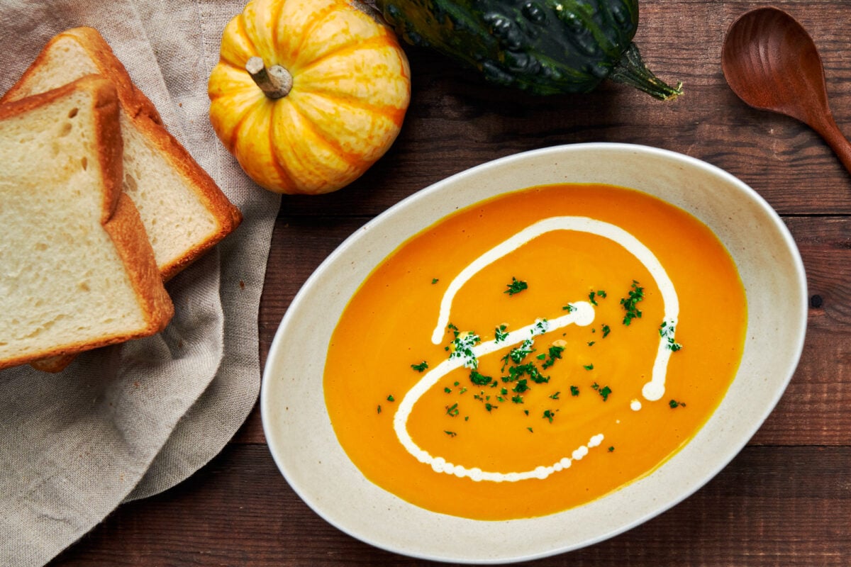 A bowl of Japanese pumpkin soup served with a drizzle of cream and a side of toast.