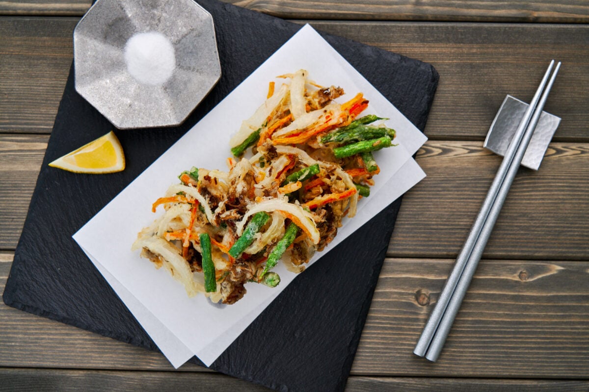 Crispy Kakiage or Japanese vegetable tempura fritters on a black slate plate served with sea salt and a wedge of lemon.