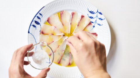 Kanpachi drizzled with olive oil being sprinkled with seasalt.