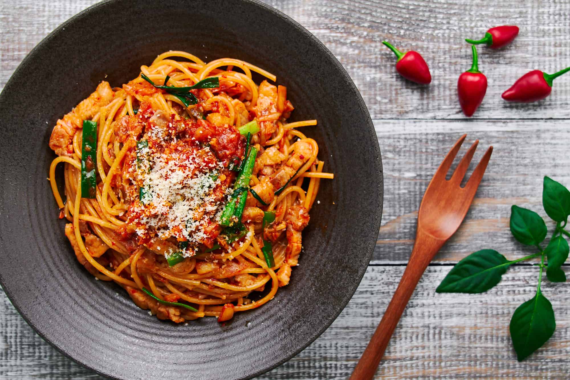 A top-down view of Pork & Kimchi Pasta, garnished with Parmigiano-Reggiano and scattered scallions.