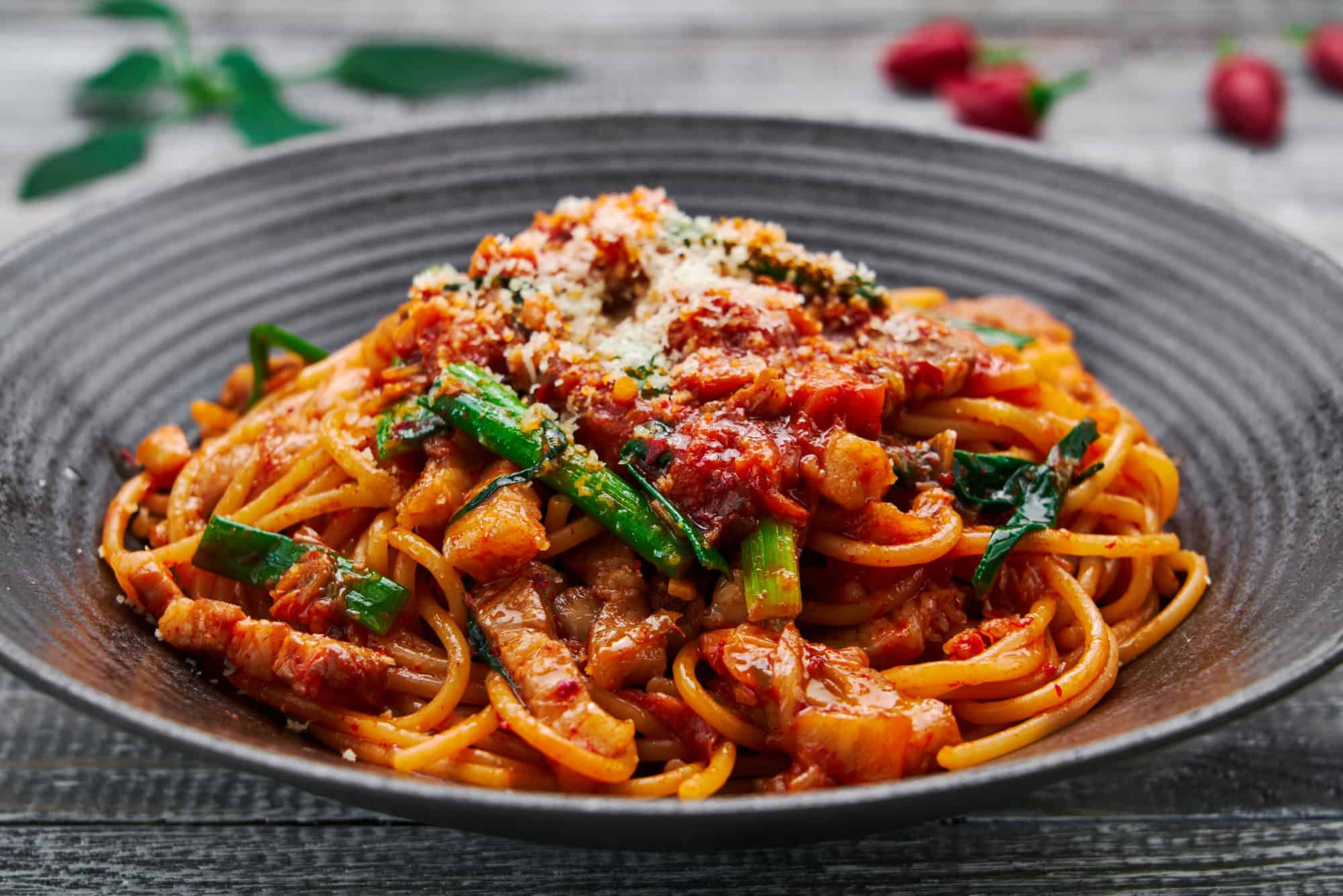 Close-up shot of juicy pork belly batons and tangy kimchi strands intertwined with al dente spaghetti, highlighting the vibrant colors and textures.