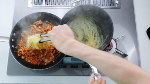 Adding spaghetti to kimchi and pork belly.