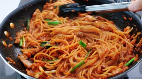 Mixing kimchi pasta with tongs.