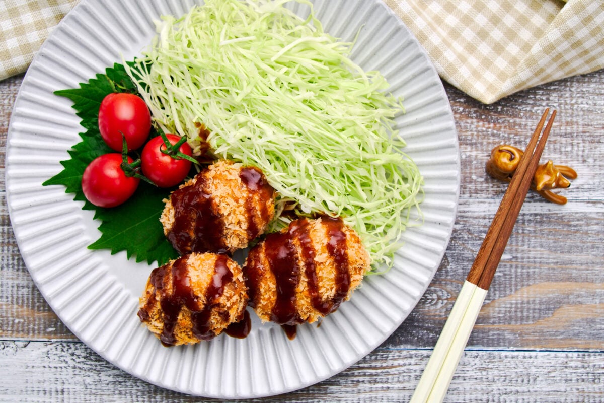 Plate of Japanese potato croquettes (korokke) with shredded cabbage salad and tomatoes.