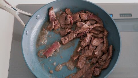 Stir-frying marinated beef in a frying pan.