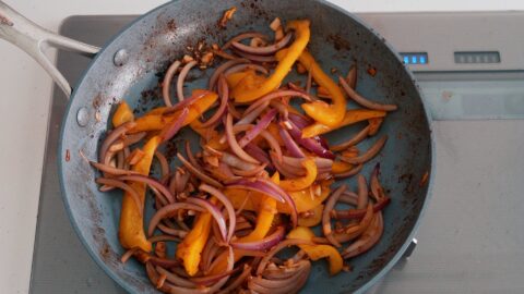 Stir-frying red onions and peppers for making Lomo Saltado.