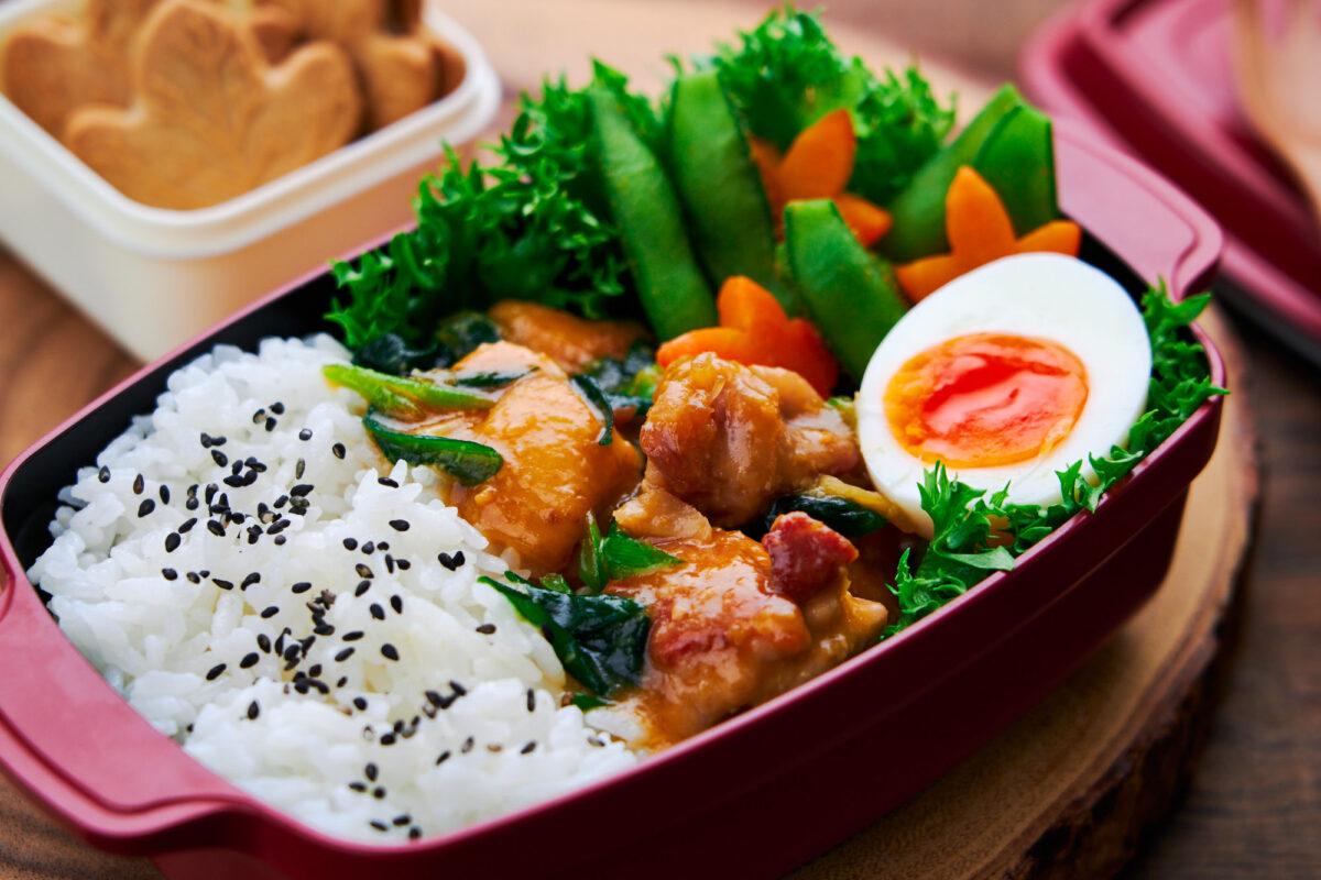 Maple Miso Chicken and rice packed into a bento box with a soft boiled egg, edamame and carrots.