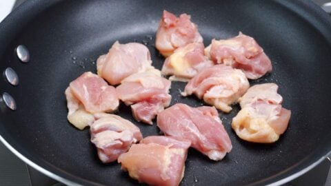 Chicken browning on the skin-side in a frying pan.