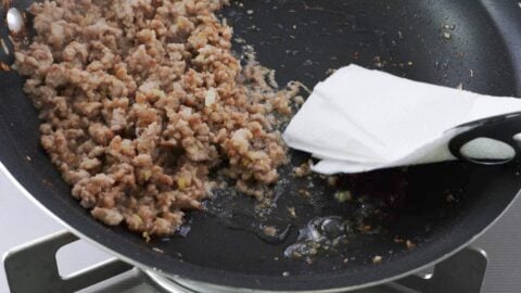 Draining excess fat from ground pork with a paper towel.