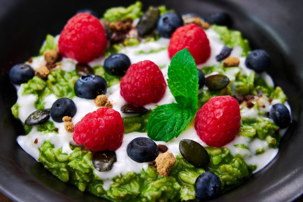 Matcha oatmeal topped with coconut cream, pumpkin seeds, raspberries, blueberries and some unrefined sugar.