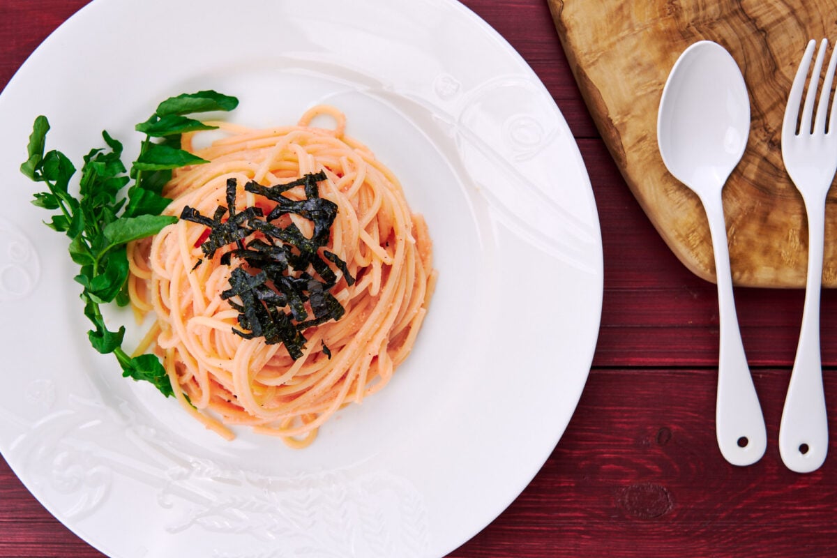 Japanese Spicy Cod Roe Spaghetti (Mentaiko Pasta) with watercress on a white plate.