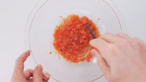 Mixing spicy cod roe and olive oil together in a glass bowl to the make mentaiko pasta sauce.