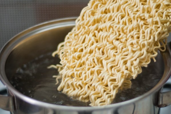 dried curly noodles entering boiling water in a pot