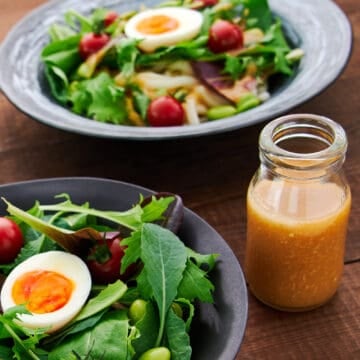 Perspective shot of a table setting showcasing Ginger Miso Dressing with a baby green salad, and the variety of dishes it pairs with, like cold noodles and poached Salmon.