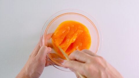 Beating eggs in a glass bowl with chopsticks.