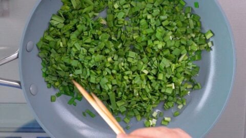 Sauteeing Nira (garlic chives) in a frying pan.