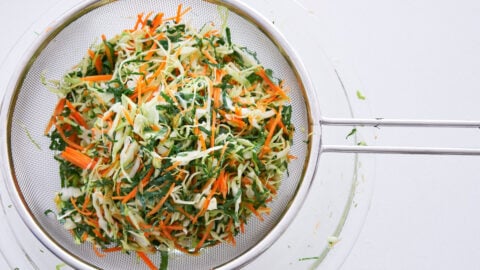 Cabbage, carrot and kale coleslaw salted and draining in a strainer.