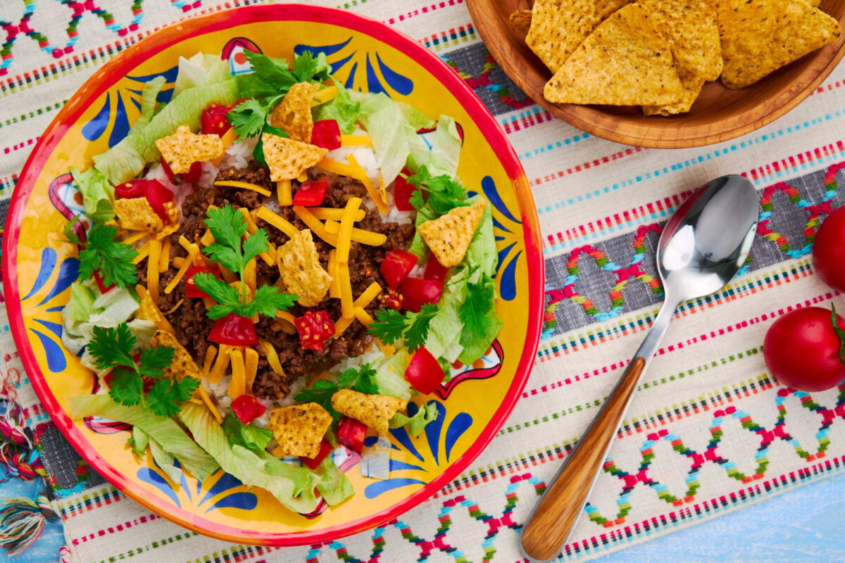 A plate of Okinawan Taco Rice with taco meat, and cheese over rice. Garnished with lettuce, tomatoes, and tortilla chips.