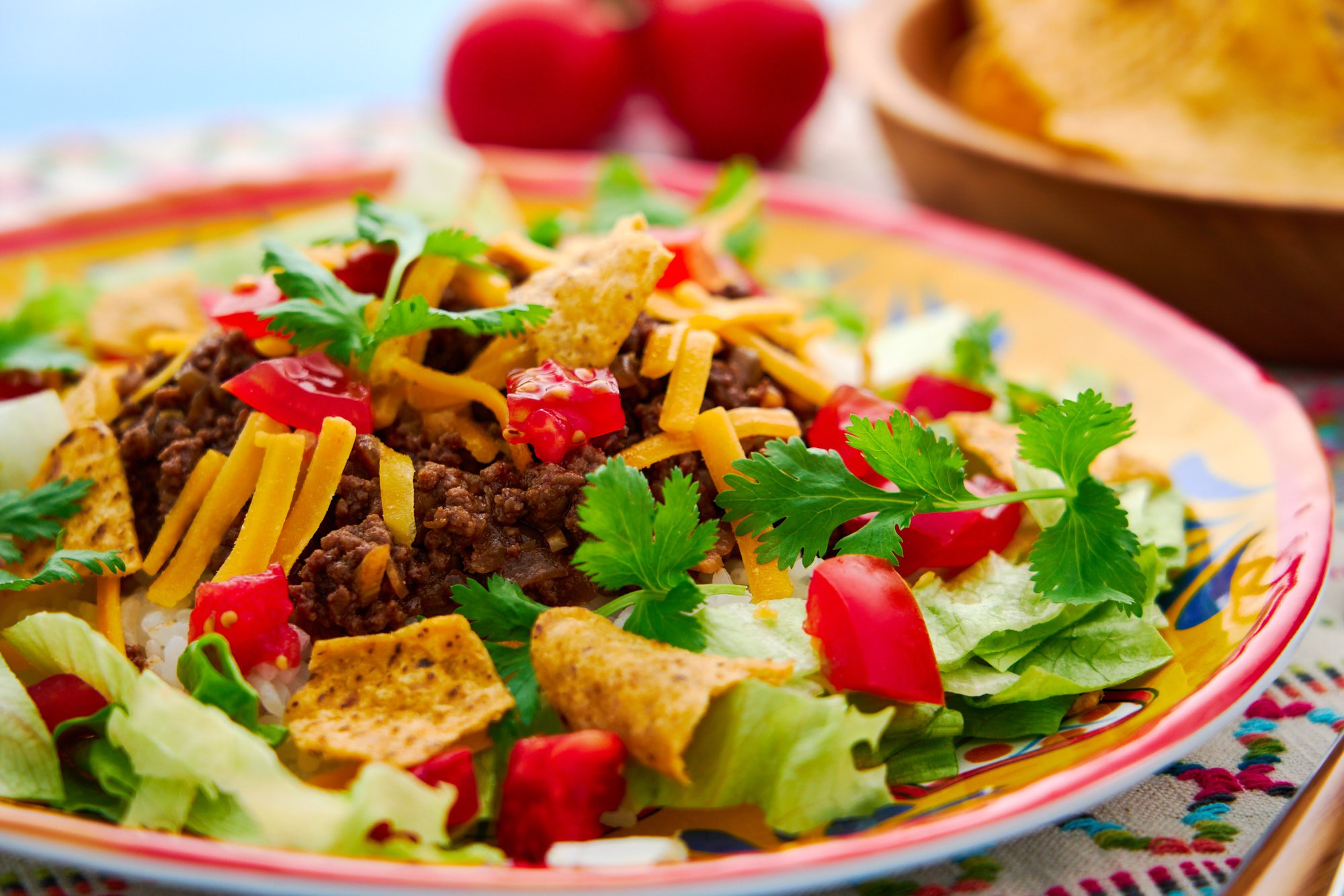 A plate Okinawan Taco Rice with layers of rice, Japanese-style taco meat, cheese, tomatoes and lettuce.