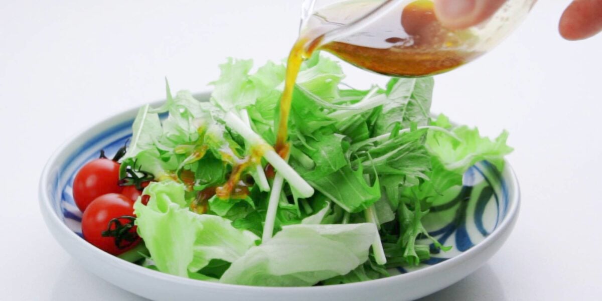 Pouring ponzu dressing over green salad.