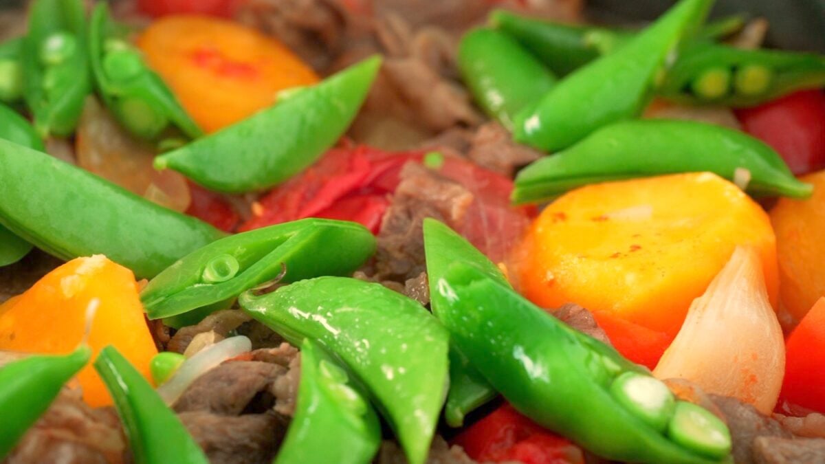 Closeup of finished Nikujaga with snap peas, potatoes, carrots, beef and tomatoes.