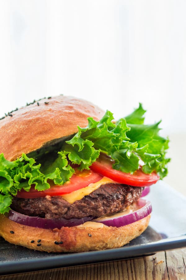 A thick, juicy hamburger patty topped with cheese, tomato, lettuce and onion, cradled in a seeded bun.