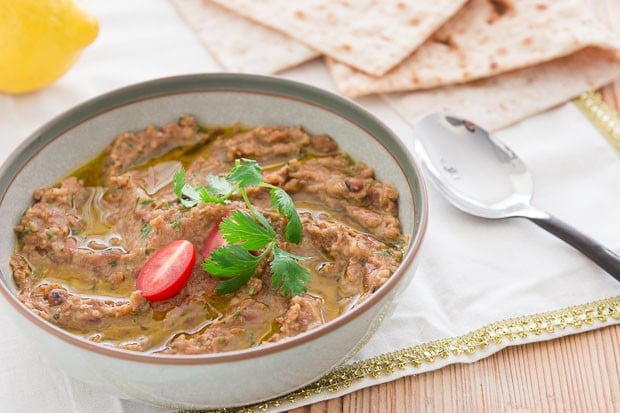 A bowl of Ful Medames anointed with olive oil and topped with tomatoes and parsley.