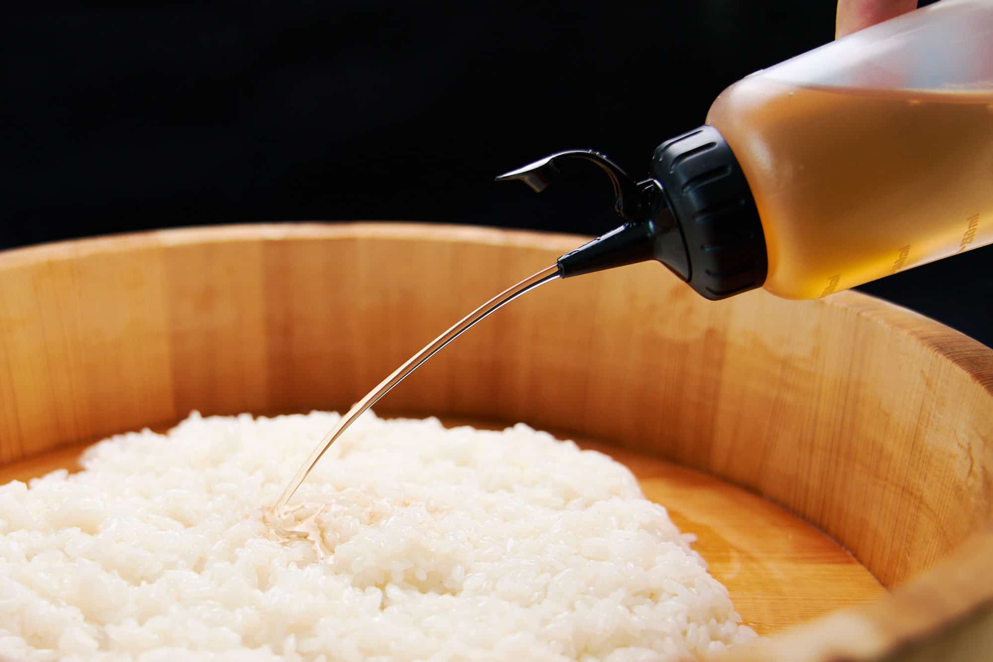 Savory, sweet, and sour seasoned sushi vinegar flows from a squeeze bottle onto a mound of Japanese sushi rice.