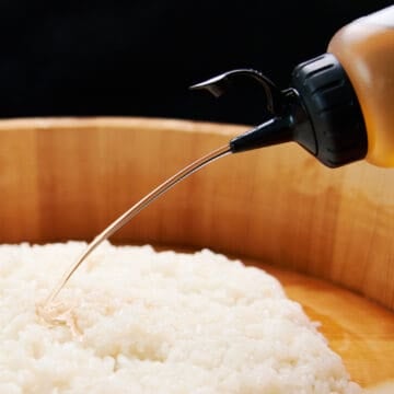 Savory, sweet, and sour seasoned sushi vinegar flows from a squeeze bottle onto a mound of Japanese sushi rice.