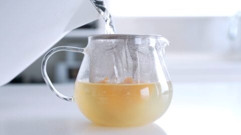 Adding boiling water to a teapot with ginger and lemon zest.