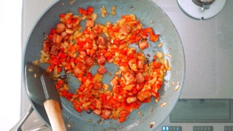 Sautéing onions and red bell peppers in a frying pan.