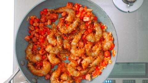 Marinated shrimp added to a frying pan with onions and red bell peppers.