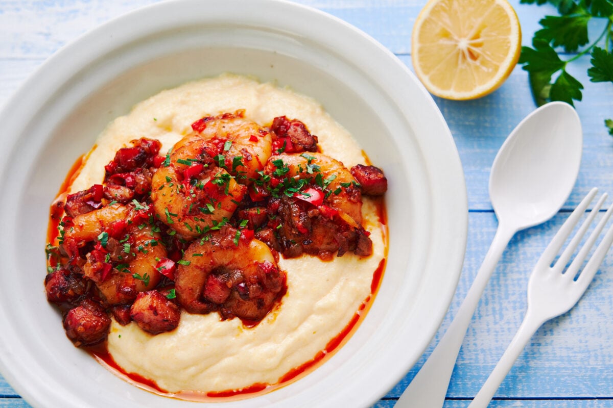 Smoky Cajun shrimp over a bed of creamy cheddar grits in a white bowl on a sky blue backdrop.