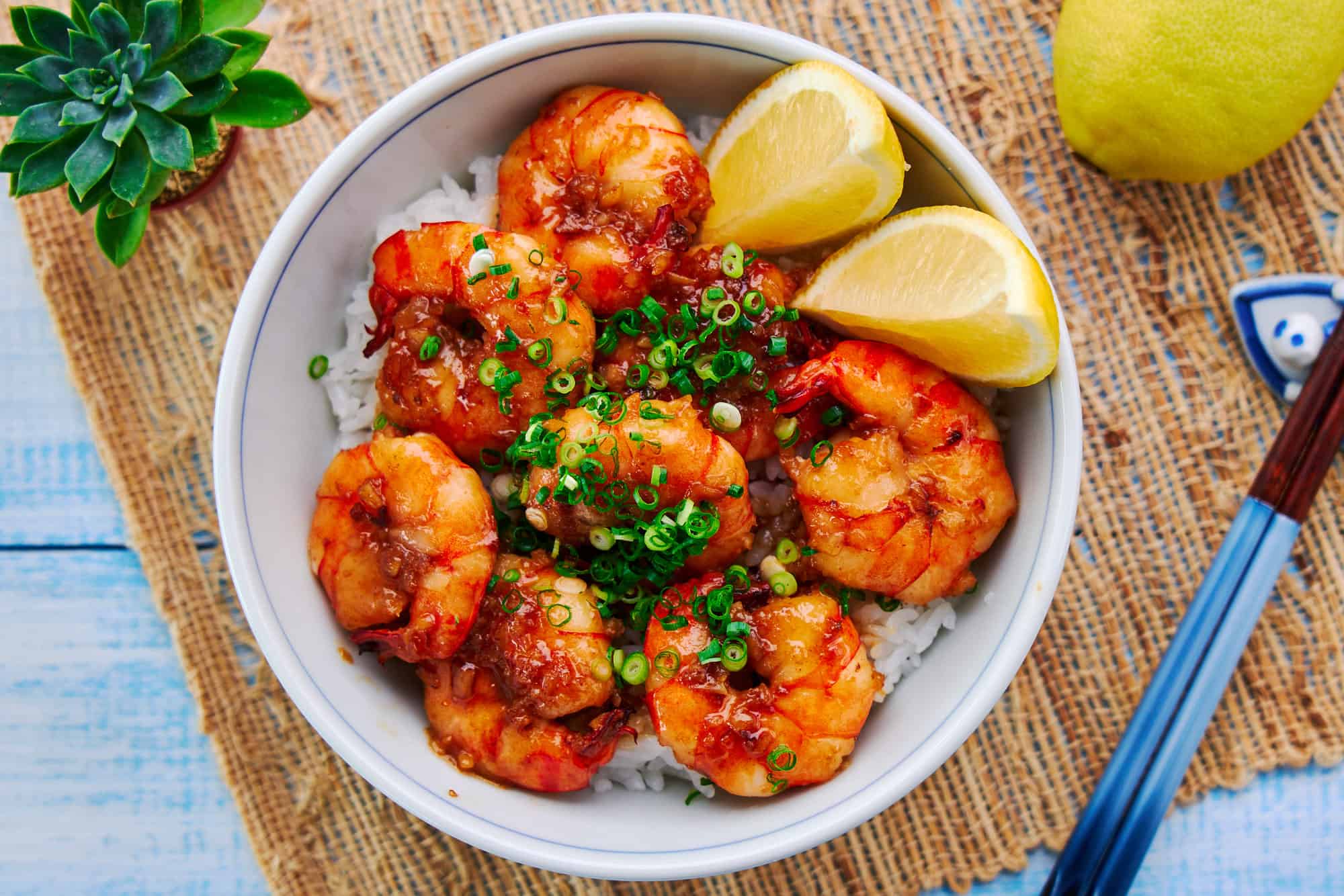 Overhead view of the Shrimp Rice Bowl, showcasing plump, golden shrimp atop steaming hot rice, garnished with fresh green scallions and a lemon wedge.