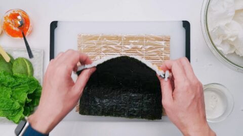 Flipping nori and rice over on a sushi mat to make an inside out sushi roll.