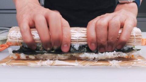 Rolling sushi roll with a bamboo sushi mat.