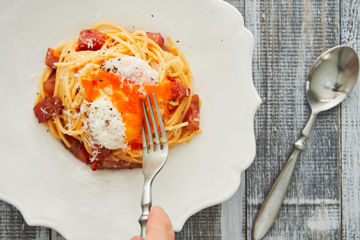 Breaking a slow cooked egg over a bowl of Spaghetti Carbonara.