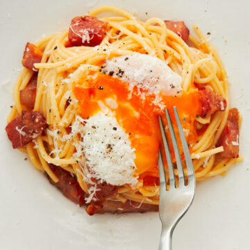 Breaking a slow cooked egg over a bowl of Spaghetti Carbonara.