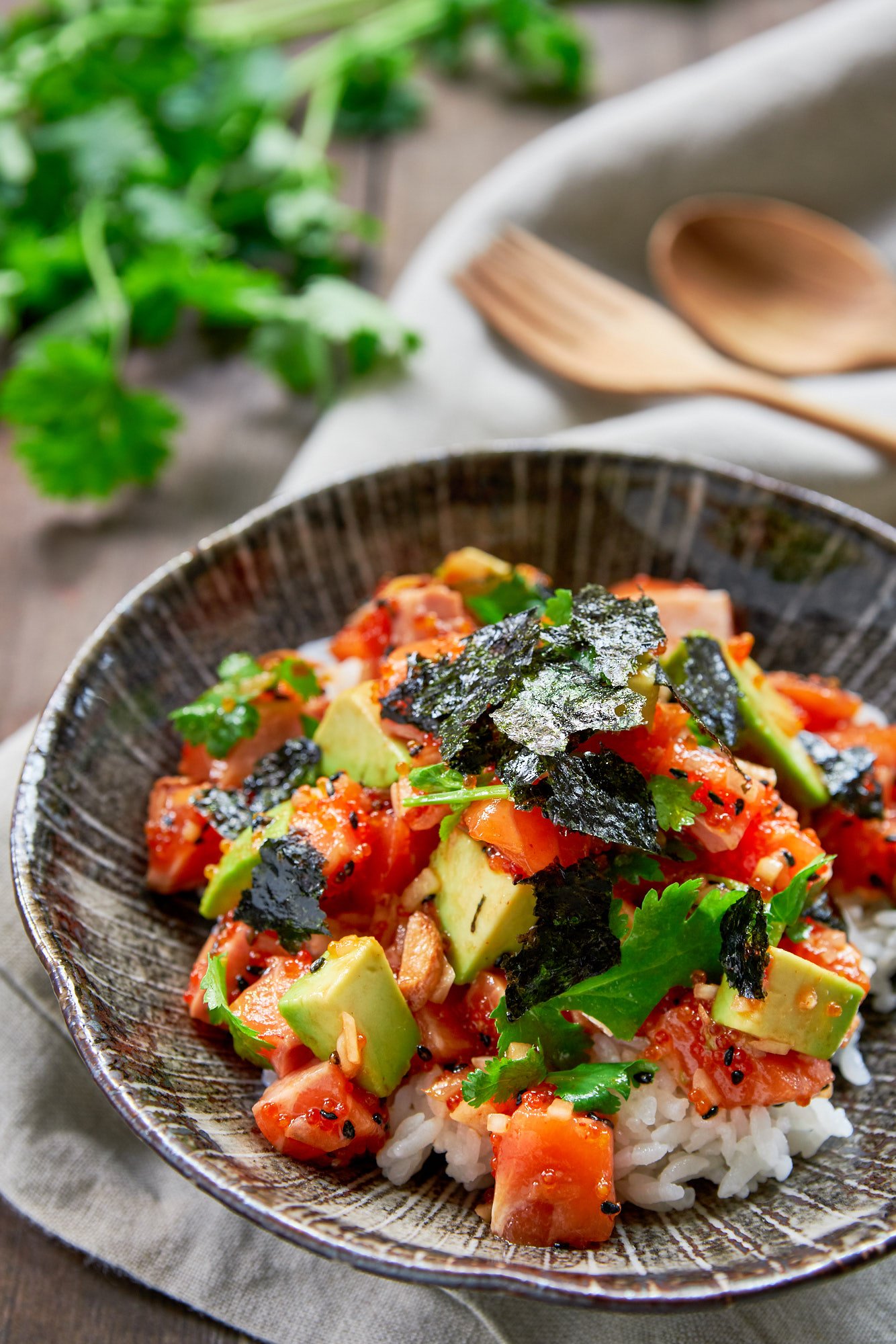 The best Spicy Salmon Poke recipe. With rich salmon, creamy avocado, crunchy tobiko, sweet onions and fresh cilantro seasoned with a sriracha sesame sauce and served over a bowl of hot rice.