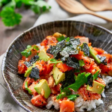 The best Spicy Salmon Poke recipe. With rich salmon, creamy avocado, crunchy tobiko, sweet onions and fresh cilantro seasoned with a sriracha sesame sauce and served over a bowl of hot rice.