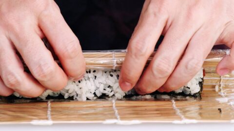 Rolling spicy tuna roll with a sushi mat.