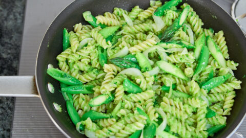 Rotini pasta tossed with green pea pesto, snap peas, spring onions and asparagus in a frying pan.