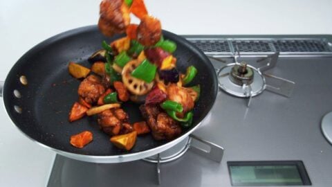 Tossing sweet and sour chicken and vegetables together in a pan.