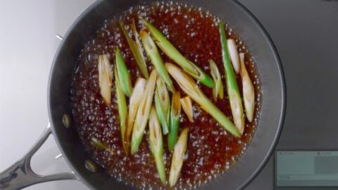 Scallions simmering in dashi stock for beef and egg rice bowl.