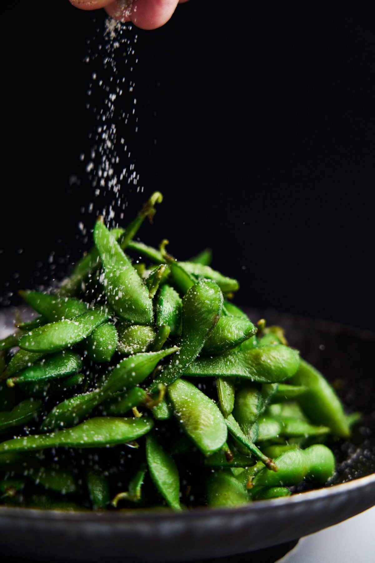 Sprinkling umami seasoning salt onto boiled edamame.