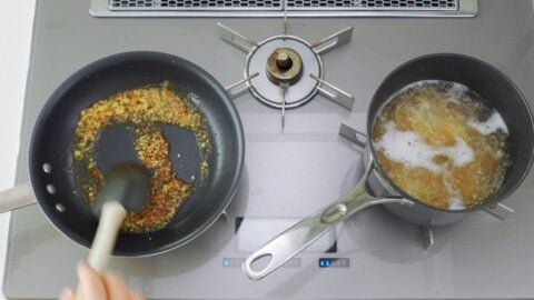 Browning soy sauce in frying pan while pasta boils on the other burner.