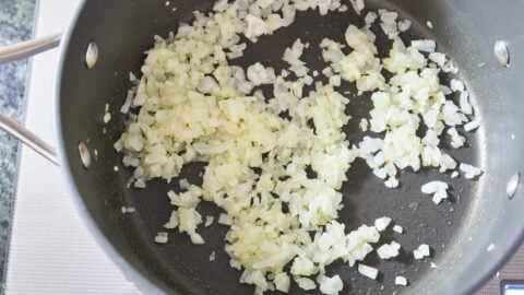 Minced onions, being sauteed in a pan on a stove for broccoli cheese soup.